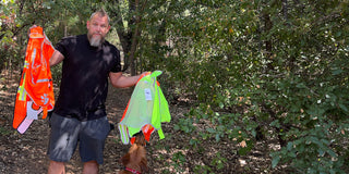 Man holding many high visibility dog vests in the woods